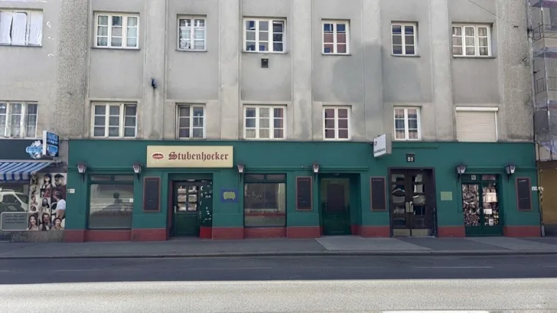 Die Fassade eines Gebäudes mit einem Geschäftslokal im Erdgeschoss und Wohnungen darüber, von der Straße aus gesehen.