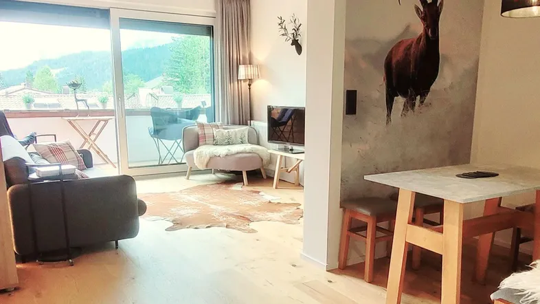 Heller Wohn- und Essbereich mit Holzboden, Balkonzugang und Bergblick.