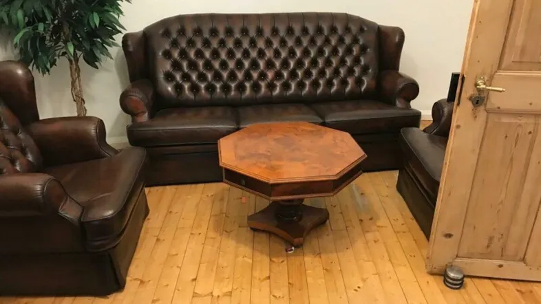 Klassisches Wohnzimmer mit Ledersofas, Holzboden und einem antiken Couchtisch, gut gepflegt.