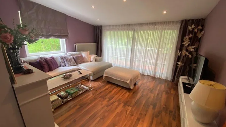 Helles Wohnzimmer mit Holzboden, gemütlichem Sofa und Zugang zu einem großen Balkon.