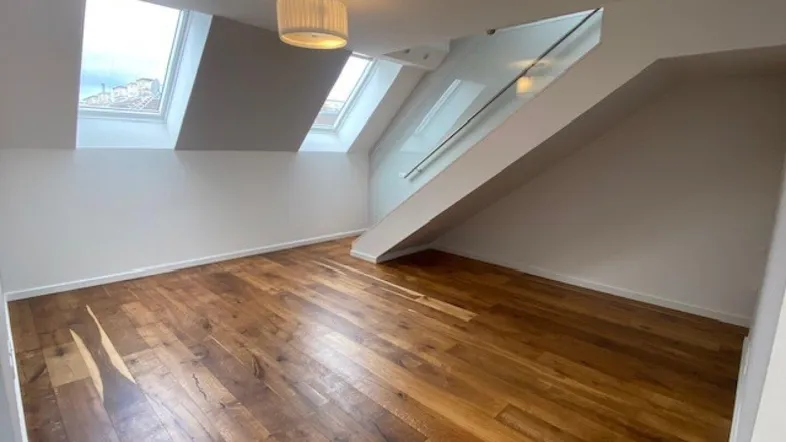 Heller Raum im Dachgeschoss mit Holzboden, Dachfenstern und offenem Treppenaufgang.