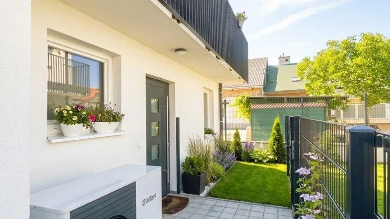 Außenansicht eines modernen Hauses mit Wärmepumpe und gepflastertem Zugang zum Garten.