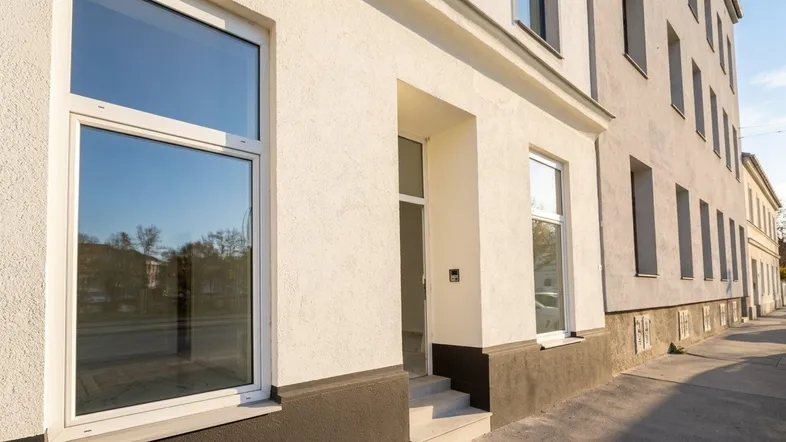 Fassade eines modernen Gebäudes mit großen Fenstern und einem einladenden Eingangsbereich an einem sonnigen Tag.