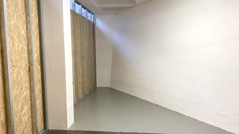 Geräumiger Lagerraum mit OSB-Plattenwänden und grauem Betonboden, der neuwertig und ungenutzt erscheint.