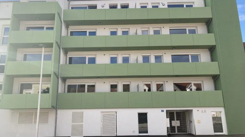 Modernes Mehrfamilienhaus mit grünen Balkonen und weißer Fassade unter blauem Himmel.