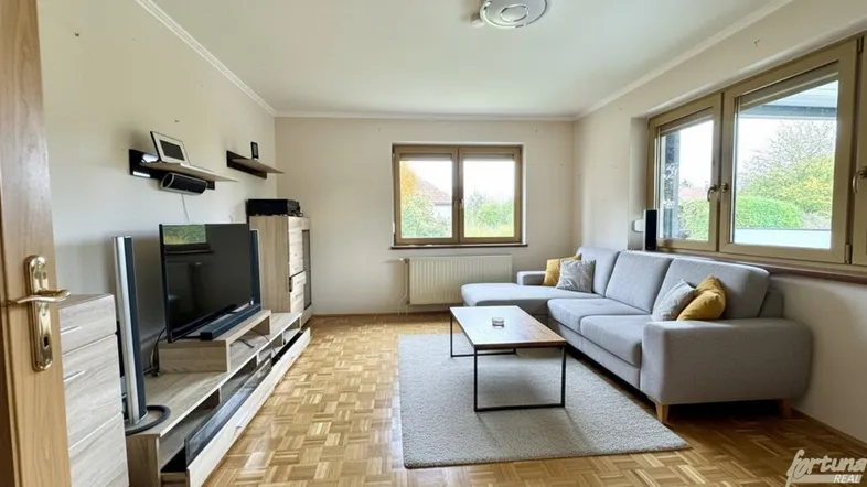 Helles Wohnzimmer mit Parkettboden, bequemer Couch und Blick ins Grüne durch große Fenster.