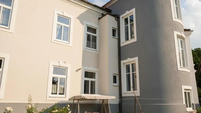 Rückansicht des Gebäudes mit geschwungener Fassade und einem gemütlichen Gartensitzplatz mit Rosen.