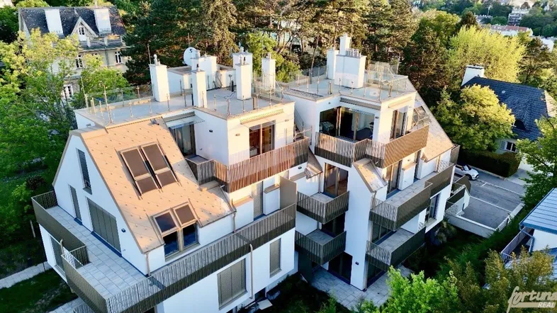 Moderne Architektur mit mehreren Balkonen und Dachfenstern, umgeben von Bäumen und viel Grün.
