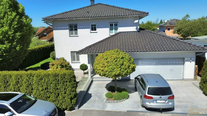 Modernes Einfamilienhaus mit weißer Fassade, dunklem Dach und gepflegter Außenanlage.