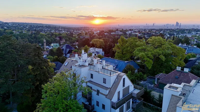 Luftaufnahme eines modernen Gebäudes bei Sonnenuntergang mit weitem Blick über die Stadt und grüne Umgebung.