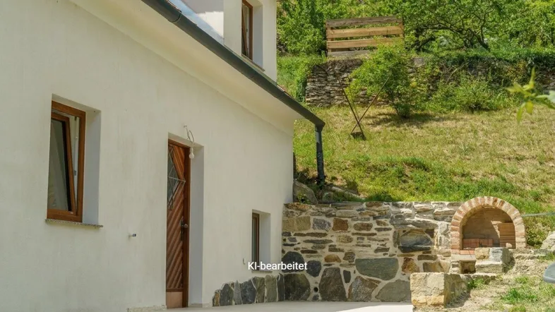 Seitlicher Blick auf das Haus mit einer kleinen Terrasse und einem traditionellen Steinofen im Freien.