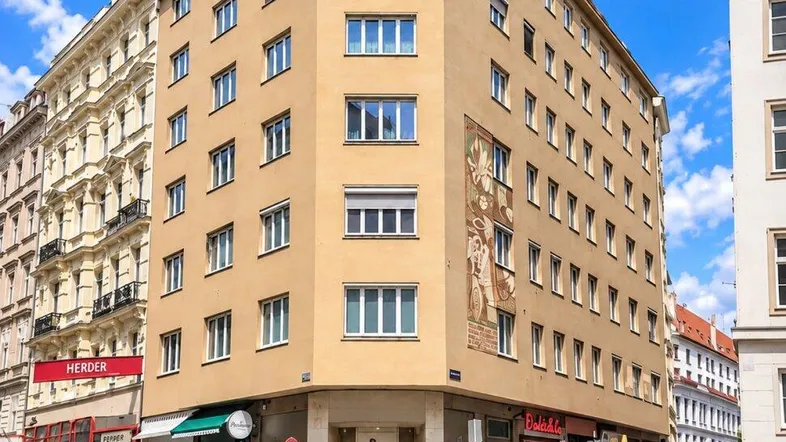 Modernes Eckgebäude in der Stadt mit Geschäften im Erdgeschoss und blauer Himmel.