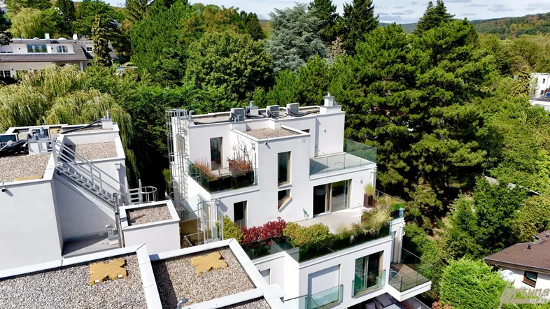 Moderne weiße Architektur mit Flachdächern und mehreren Terrassen, umgeben von üppigem Grün.