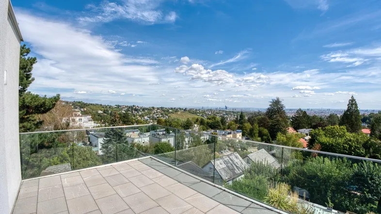 Geräumige Terrasse mit Steinplatten und Glasgeländer bietet einen weiten Blick über die Stadt und Landschaft.