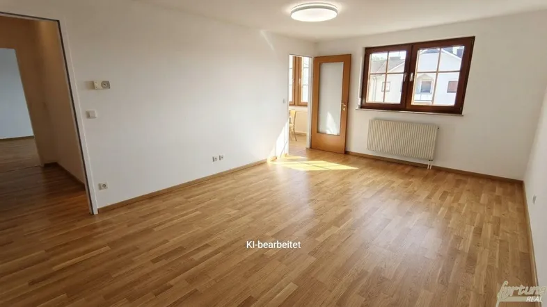 Helles Wohnzimmer mit Holzboden, weißen Wänden und einem großen Fenster mit Heizkörper.
