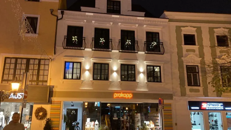 Beleuchtete Fassade des Gebäudes bei Nacht mit festlicher Dekoration an den Balkonen.