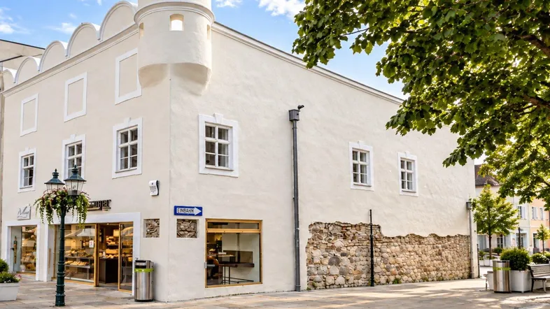 Historisches Gebäude mit markantem Eckturm und Bäckerei im Erdgeschoss an einer belebten Straße.