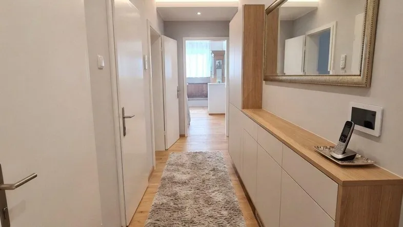 Heller Flur mit Holzfußboden, einem langen Teppich und einem großen Spiegel, der den Raum optisch erweitert.