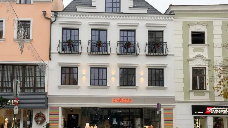 Moderne Fassade eines Mehrfamilienhauses mit Geschäften im Erdgeschoss und dekorativen Balkonen.