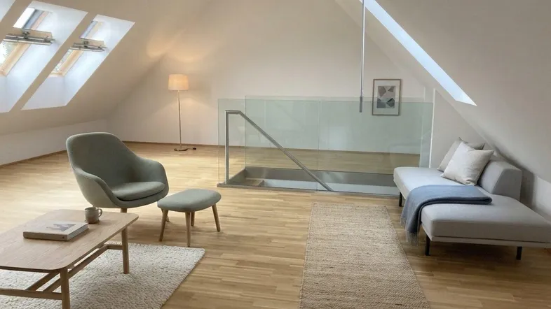 Heller Wohnbereich im Dachgeschoss mit schrägen Decken, Dachfenstern und modernem Holzfußboden.