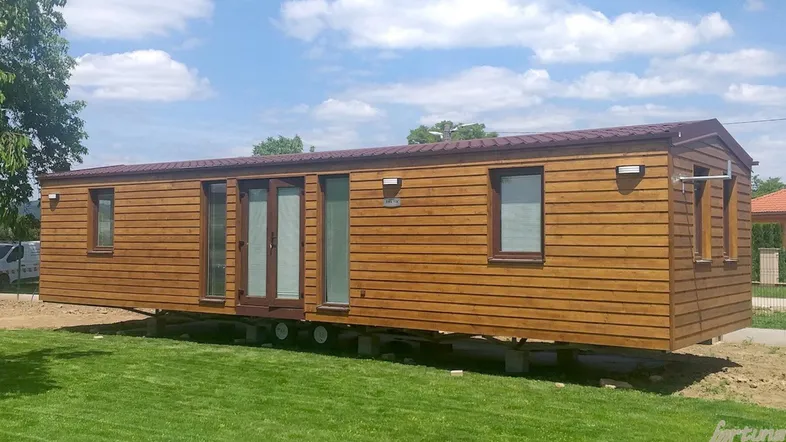 Außenansicht eines modernen Holz-Mobilheims auf einem grünen Rasen unter blauem Himmel.