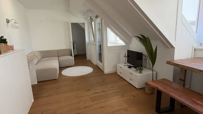 Helles Wohn- und Esszimmer mit Holzboden, gemütlichem Sofa und Dachschrägen.
