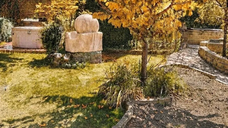 Gepflegter Gartenbereich mit Herbstlaub, Steinweg und dekorativen Elementen unter einem Baum.