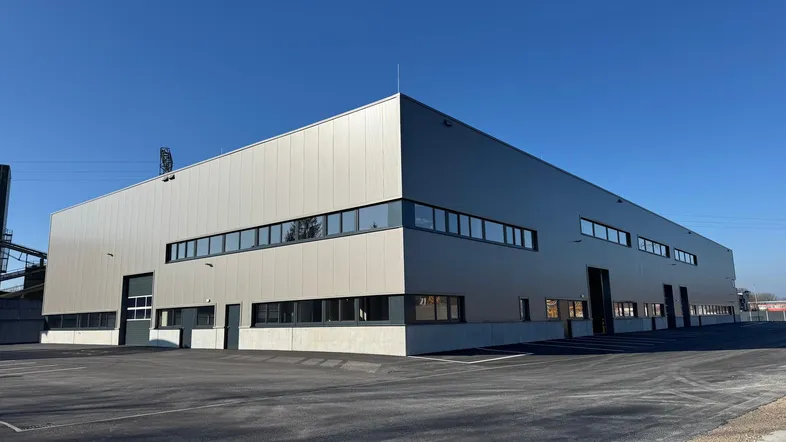 Modernes Industriegebäude mit heller Fassade und großem Parkplatz unter blauem Himmel.