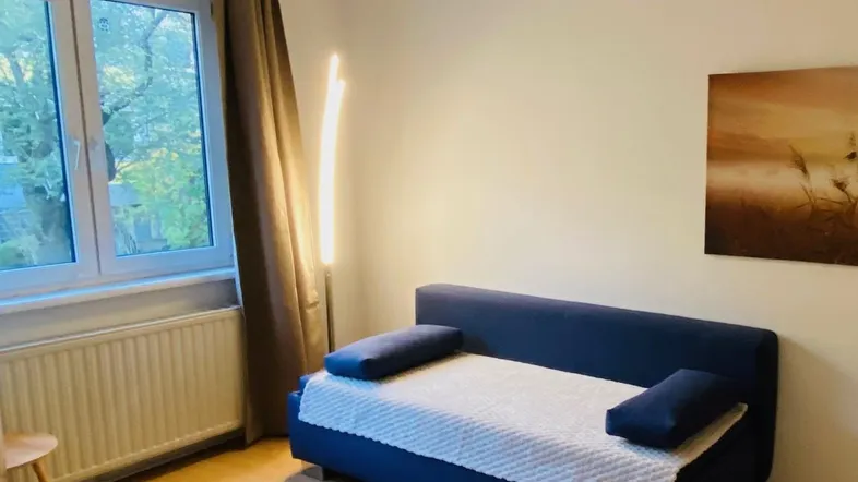 Helles Wohnzimmer mit blauem Sofa, Holzboden und einem Fenster mit Blick ins Grüne.