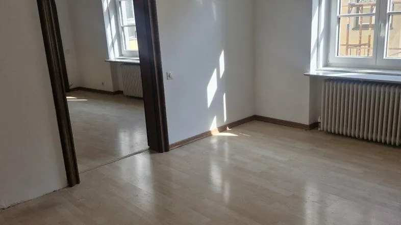 Heller, leerer Raum mit Laminatboden, weißen Wänden und Rundbogen-Durchgang zu einem weiteren Zimmer.
