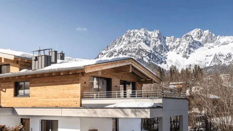 Modernes Chalet mit Holzfassade und Balkonen vor einer beeindruckenden Bergkulisse im Winter.