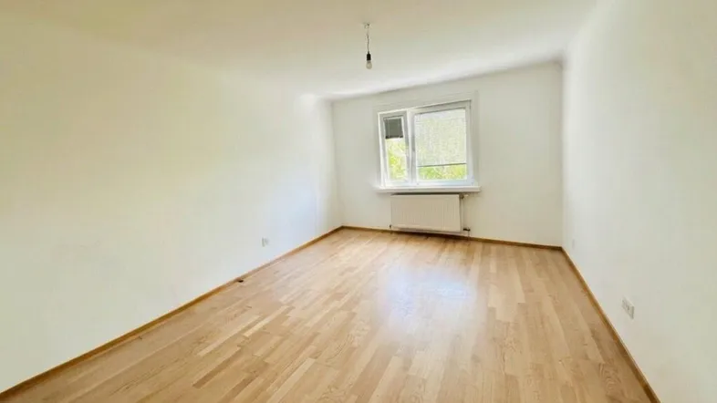 Helles, leeres Zimmer mit Parkettboden und weiß gestrichenen Wänden, bereit zur individuellen Gestaltung.