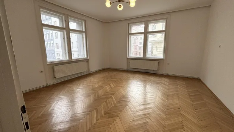 Helles Wohnzimmer mit klassischem Fischgrätparkett, großen Fenstern und moderner Deckenleuchte.