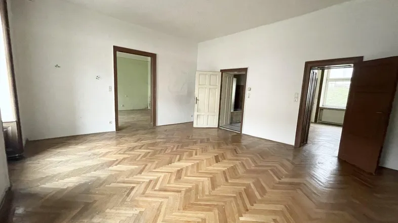 Geräumiges Zimmer mit Fischgrätparkett und mehreren Türöffnungen, bereit zur Renovierung.
