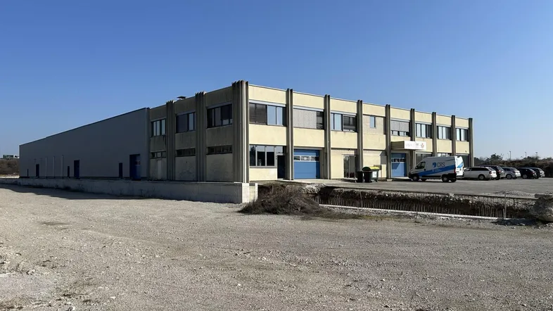Großes Industriegebäude mit Büroflächen und Lagerhallen auf einem weitläufigen Gelände unter blauem Himmel.