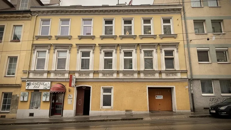 Gelbe Fassade eines Mehrfamilienhauses mit vielen Fenstern und einem Geschäft im Erdgeschoss.