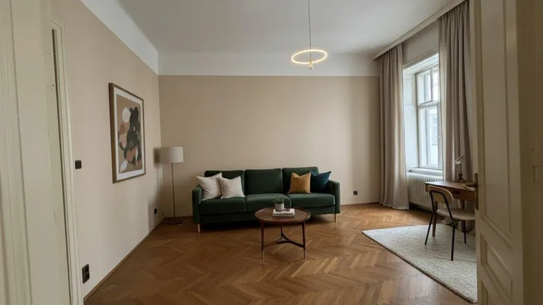 Helles Wohnzimmer mit Fischgrätparkett, beigefarbenen Wänden und einem grünen Sofa.