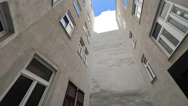 Blick in einen engen Innenhof zwischen zwei Gebäudeflügeln mit vielen Fenstern und natürlichem Licht.