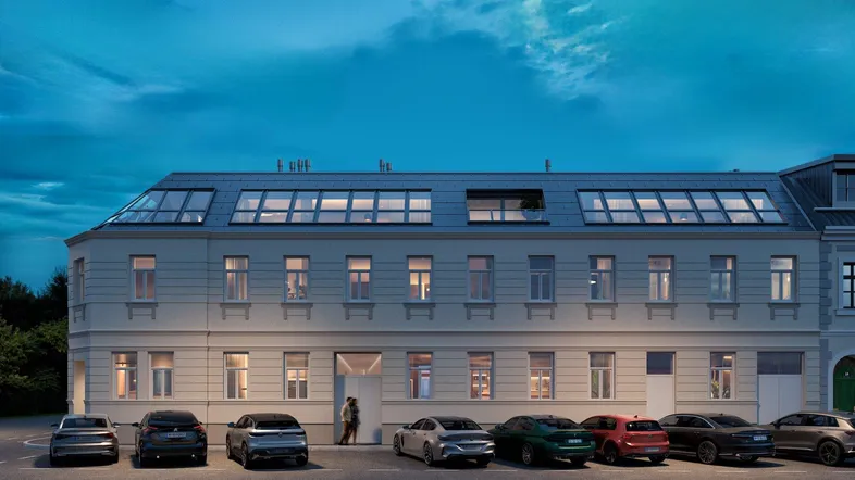 Moderne Gebäudefassade bei Dämmerung mit vielen Fenstern und Mansarddach.