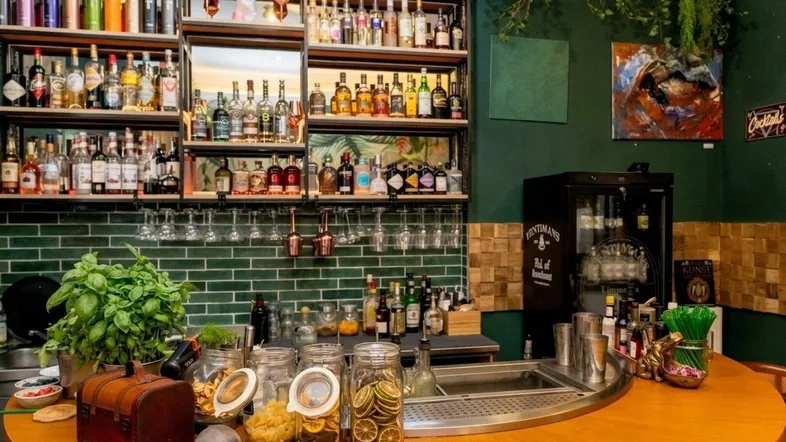 Detailansicht der Bar mit frischen Kräutern, Gläsern und einer großen Auswahl an Getränken auf den Regalen.