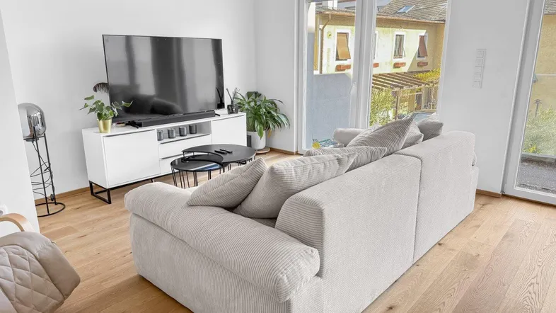 Helles Wohnzimmer mit modernem Sofa, TV-Möbel und Zugang zu einem Außenbereich.