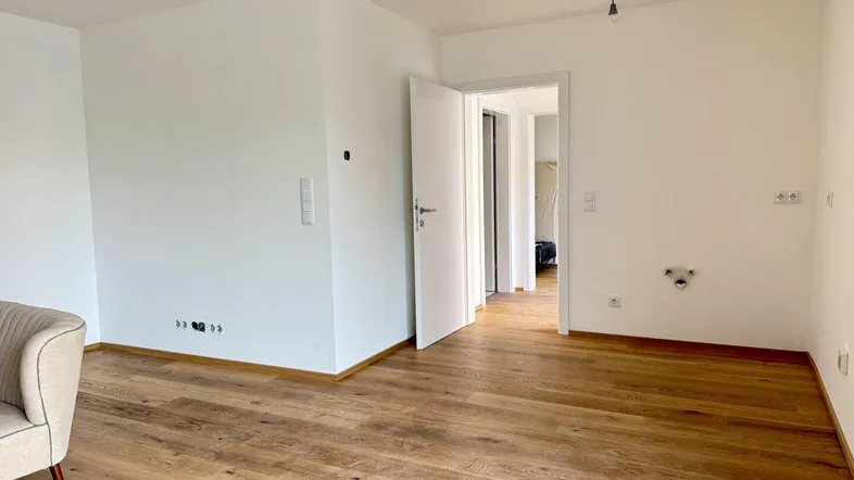 Helles, leeres Zimmer mit Holzboden und weiß gestrichenen Wänden, bereit zur Einrichtung.