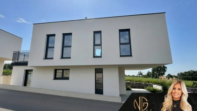 Moderne weiße Doppelhaushälfte mit großen Fenstern und Balkon unter blauem Himmel.