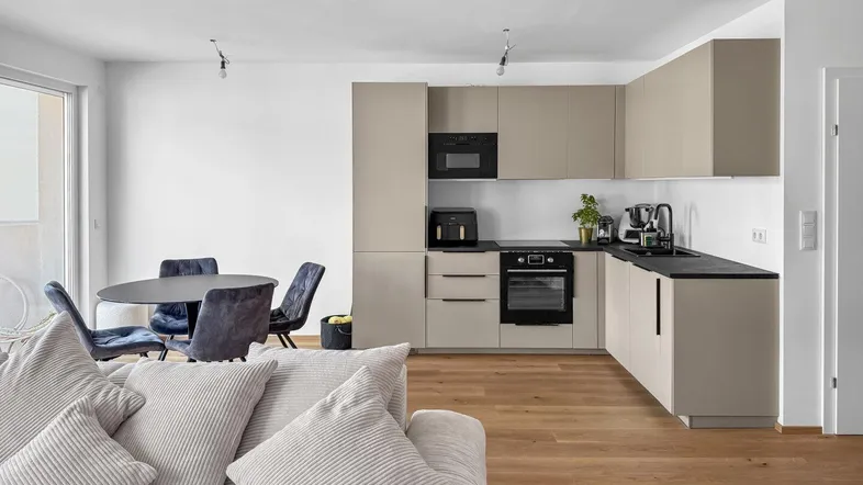 Moderner offener Wohn-Essbereich mit integrierter Küche, Holzboden und bequemer Couch.