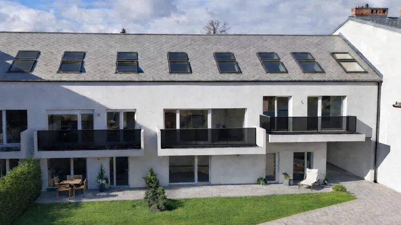 Moderne Wohnanlage mit mehreren Balkonen, Terrassen und kleinen Gärten unter einem Schrägdach.