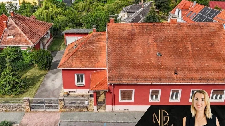 Luftaufnahme eines roten Hauses mit Ziegeldach, umgeben von viel Grün und weiteren Gebäuden.