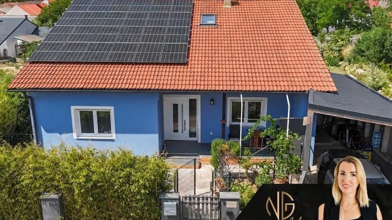 Blaues Einfamilienhaus mit rotem Ziegeldach, Solaranlage und gepflegtem Vorgarten.
