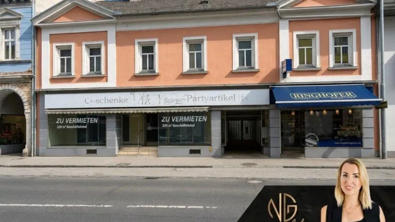 Die Fassade eines älteren Gebäudes mit Geschäftsflächen im Erdgeschoss und Wohnungen darüber, direkt an der Straße gelegen.