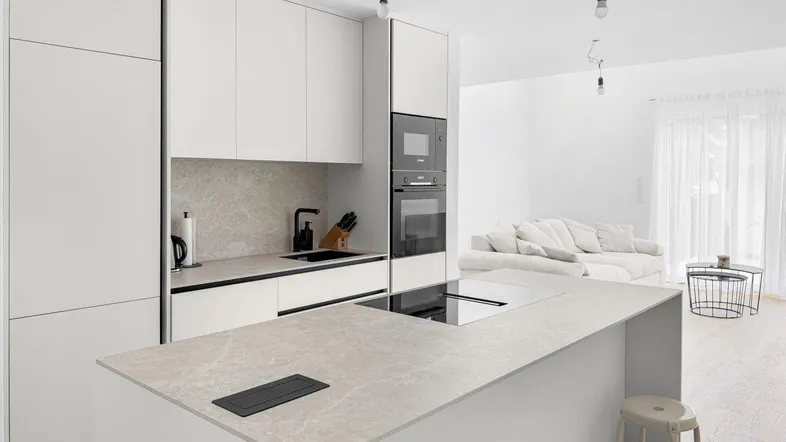 Moderne, offene Küche mit weißer Einbauküche, Kochinsel und Blick in den Wohnbereich.