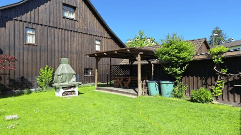 Großer Garten mit Rasenfläche, überdachtem Sitzbereich und Grillplatz hinter dem Holzhaus.